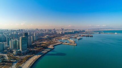 Fototapeta premium Aerial View of Urban Skyline Next to the Coastline Featuring Modern Buildings, Boats, and a Clear Blue Sky with Few Clouds in the Background