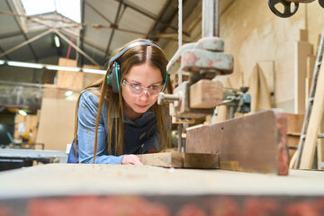 Focused young woman learning woodworking skills in a lumberyard