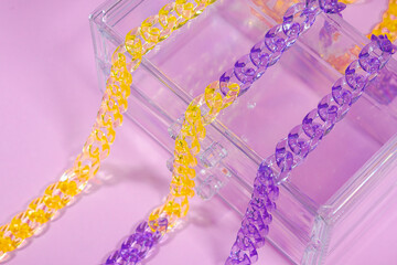 Colorful, translucent plastic chains laid out in a row on a pink background.
