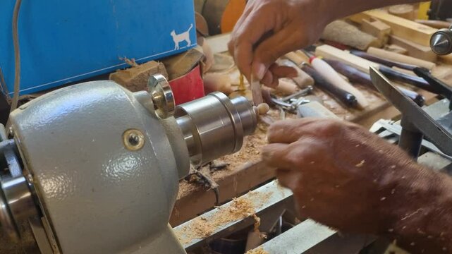 closeup of mans hand rubbing sanding paper agains wooden toy spinning fast on lathe