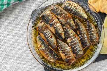 Sardines arranged in an ornate glass bowl filled with oil, displayed on a light-colored woven placemat, capturing rustic culinary elegance.