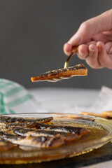 Sardines arranged in an ornate glass bowl filled with oil, displayed on a light-colored woven placemat, capturing rustic culinary elegance.