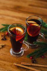Two glasses of christmas mulled wine with oranges and spices on wooden background