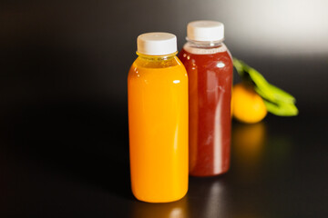 two transparent bottles with red and orange fruit drink on a black background