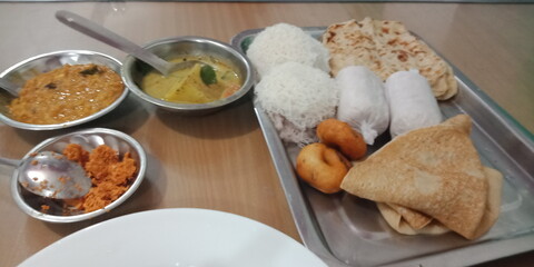 An Asian-style platter of string hoppers, pittas, ulunthu vadai, and parathas. They are accompanied by a well-seasoned lentil curry, a potato stew, and a red coconut sambol. Indian style Street food