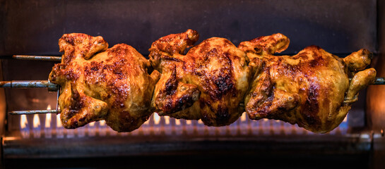 Close-up of a roasted chicken turning on a spit in a rotisserie oven, showcasing its crispy, golden-brown skin with flames flickering in the background for a perfect culinary vibe. © Samir