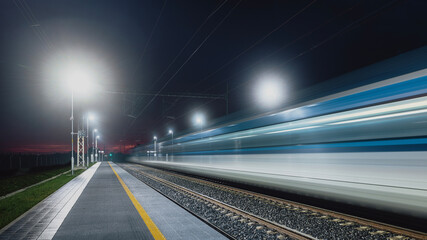 Modern railway at night. Light trail of high speed train in railroad station. Moving modern intercity passenger train.