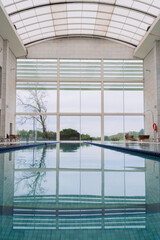 Symmetrical indoor swimming pool with lanes and a modern glass ceiling, offering a peaceful view of the surrounding greenery