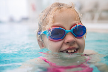 Girl wearing colorful goggles smiling in a swimming pool on a sunny day