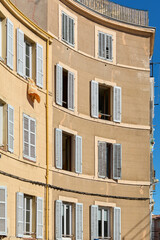 A curved building facade in Marseille with multiple shuttered windows, some open, capturing the charm of historic architecture on a sunny day.