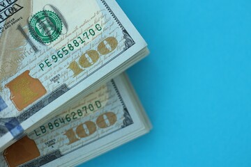 Big amount of hundred dollar bills in thick stack lies on bright blue color paper background