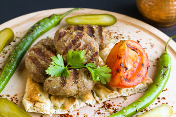 Grilled meatballs designed on wooden tray with tomato,pepper,parsley and cucumber pickles on black surface 