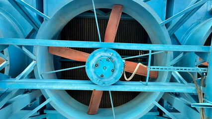 На фотографии современный вентилятор синего цвета с желтым цветом детали на нем  для охлаждения оборудование на открытом воздухе