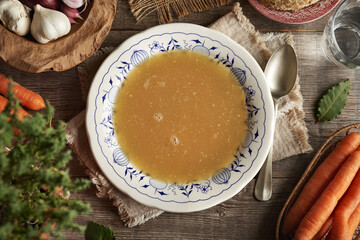 Chicken bone broth in vintage plate with ornaments on a rustic table
