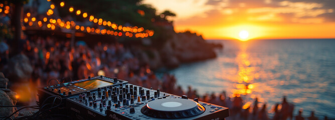 A close-up shot of hands on turntables, with people dancing in soft focus behind at sunset during an outdoor party. A photo of DJ equipment on the beach with a sunset and crowd in the background.