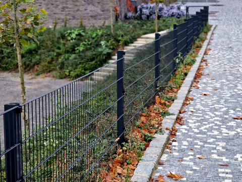 The park's beautiful lawn is protected from the entrance from the street by a low fence made of gray galvanized steel. gate and gate for gardener maintenance entrance