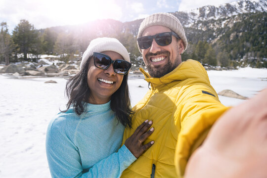 Young cheerful multiracial couple taking selfie photo in the snow trip in winter