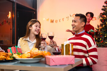 Two handsome men and two beautiful women laugh joyfully while celebrating Christmas. They enjoy delicious food, drinks, exchange gifts in a lively atmosphere, creating unforgettable festive memories
