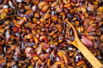 Chopped raw plums boiling for jam cooking process, with a wooden spoon
