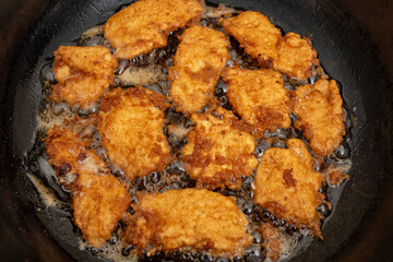 Chicken breast meat fillets with egg in boiling oil in a pan, flat lay close up