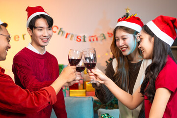 Two handsome young men and two beautiful young women wearing Christmas hats laughing joyfully at a Christmas party with delicious food, drinks and a cheerful exchange of thoughtful gifts