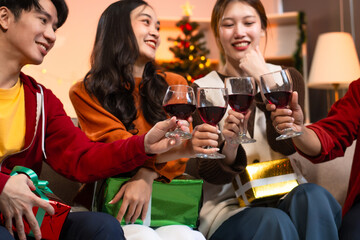 Two handsome young men and two beautiful young women wearing Christmas hats laughing joyfully at a Christmas party with delicious food, drinks and a cheerful exchange of thoughtful gifts