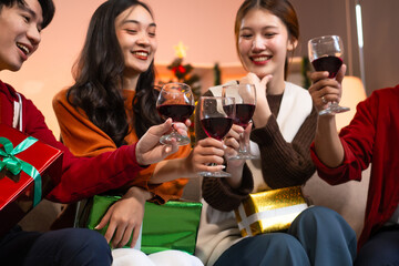 Two handsome young men and two beautiful young women wearing Christmas hats laughing joyfully at a Christmas party with delicious food, drinks and a cheerful exchange of thoughtful gifts