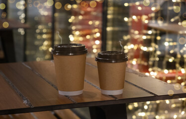 Hot coffee cup on wood table in christmas night party. light bokeh of christmas tree blur background with snow.