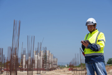 Asian architect engineer wearing safety uniform surveying and working at building structure checking blueprints construction site road general job details business concept architecture street