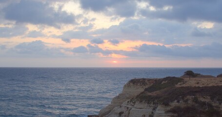 A breathtaking sunset gracefully blankets the vast ocean, beautifully framed by majestic cliffs and soft, fluffy clouds, perfectly capturing the serene and magical beauty of this moment