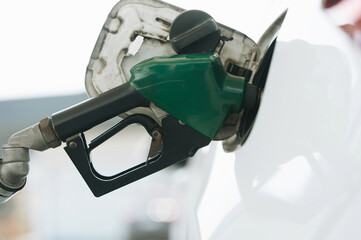 White car refueling at gas station with green fuel nozzle.