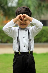 cute little boy forming heart shape from his hands. adorable 4 year old boy wearing formal outfit with Bow tie and suspenders. valentines day special romantic pose by a boy. expressing love with smile