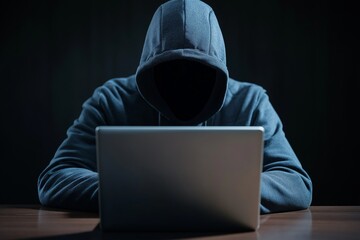 Hooded figure on a laptop in a dark room. Ideal for cybersecurity and tech thriller concepts