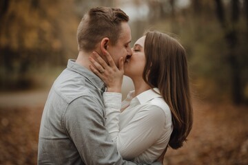 Fototapeta premium Young couple kissing in autumn park showing love and affection