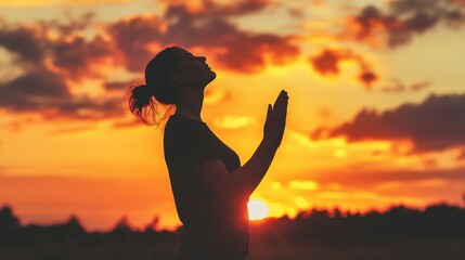 Fototapeta premium A woman is praying in a field at sunset. She is holding her hands up in the air