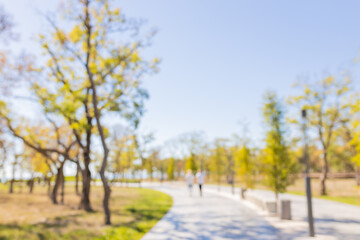 Blurred background of people walking on a scenic path among trees in a park during sunny weather in autumn