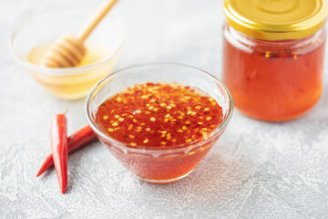 Hot honey in bowl and  chili peppers on grey background
