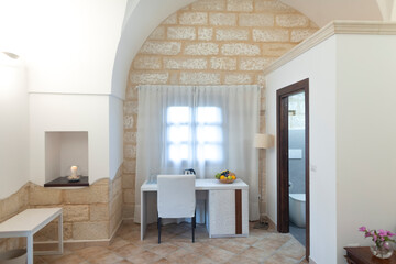 This modern workspace features sleek white furniture, a stunning stone wall, and plenty of natural light, ideal for enhancing productivity and enjoyment during relaxation