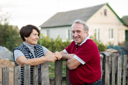 Positive mature man and woman standing near fence in garden - Powered by Adobe