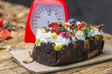   Close-up of a beautifully decorated dessert loaf cake with a rich texture, adorned with cream, fresh strawberries, and colorful chocolates. Set on a rustic table with natural elements.