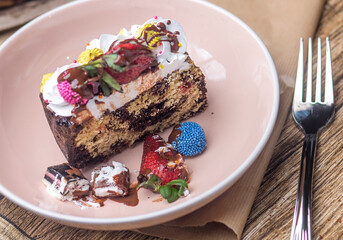   Close-up of a beautifully decorated dessert loaf cake with a rich texture, adorned with cream, fresh strawberries, and colorful chocolates. Set on a rustic table with natural elements.
