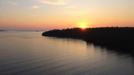 Obraz premium Sunset over the calm waters of a wooded peninsula, ocean, bay