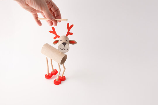 DIY reindeer puppet made from cardboard tubes, red plastic caps, and paper details. Studio shot on white background. Holiday craft and decoration concept. Fun eco-friendly project for kids