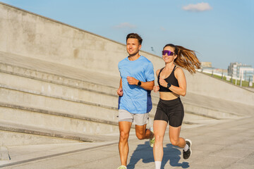 Fototapeta premium Two Runners Jog Together on a Sunny Day in an Urban Park Setting Near Modern Buildings