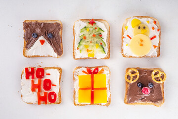 Obraz premium Christmas funny creative toasts sandwich for kids breakfast. Homemade Christmas morning sandwiches in form of gift, Christmas tree, deer, snowman, penguin, with cheese, fruit, chocolate, vegetables
