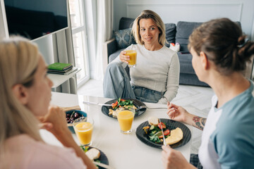 A group of female friends sitting at the table having breakfast and chatting.