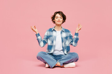 Full body young woman wear blue shirt white t-shirt casual clothes sits hold hands in yoga om aum gesture relax meditate try to calm down isolated on plain pastel pink background. Lifestyle concept.