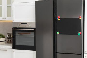 Fototapeta premium Blank note board with magnets on refrigerator in kitchen. Mockup for design