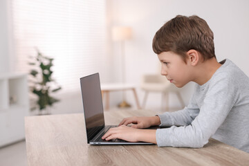 Boy with incorrect posture using laptop at wooden desk indoors