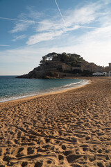 Golden sandy beach with turquoise waves gently lapping the shore, overlooked by a historic fortress...